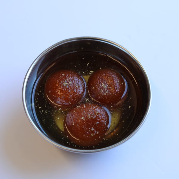 Three gulab jamun, Indian fried dough balls soaked in syrup, in a metal bowl.