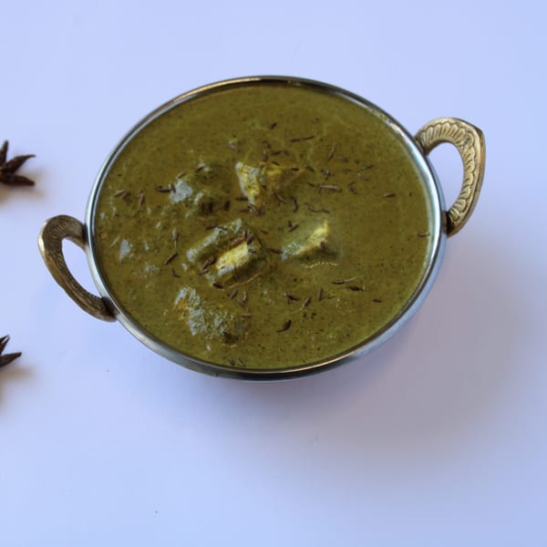 Palak Paneer, a vibrant green Indian spinach and cheese curry, in a decorative metal bowl.