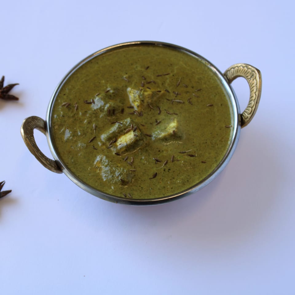 Palak Paneer, a vibrant green Indian spinach and cheese curry, in a decorative metal bowl.