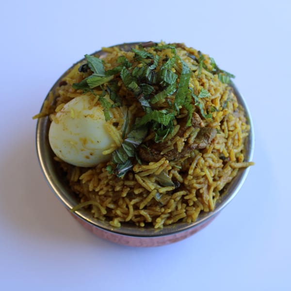Indian biryani with rice, meat, a hard-boiled egg, and fresh mint in a copper bowl.