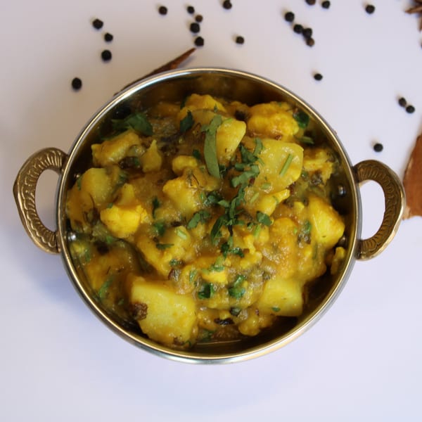 Curry On Indian Cuisine's Aloo Gobi, a potato and cauliflower curry, in a traditional brass bowl.