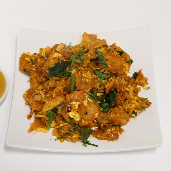 Indian Kothu Parotta, a chopped flatbread dish with scrambled egg and herbs, on a white plate.