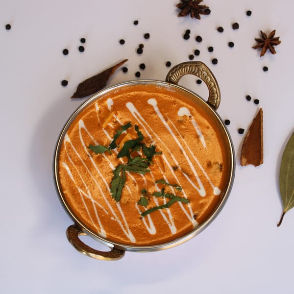 Indian butter chicken in a metal bowl, garnished with cream and cilantro, surrounded by spices.