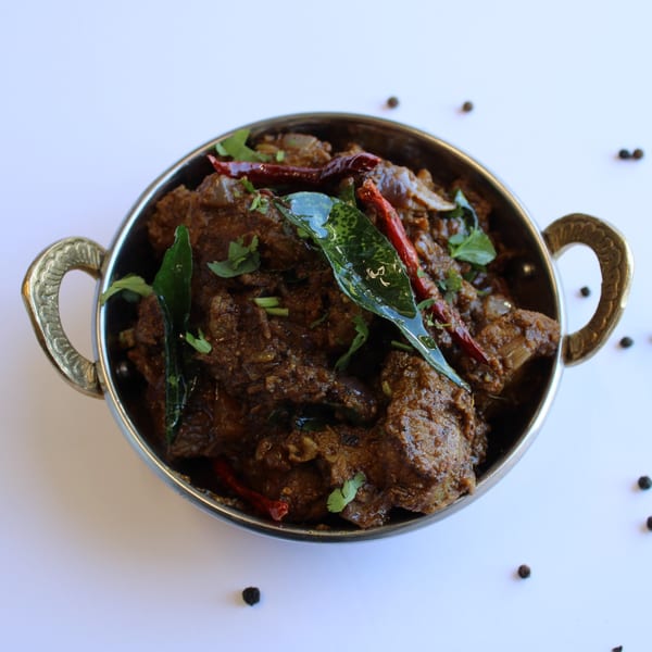 Curry On Indian Cuisine's dark Indian curry with red chilies and green herbs in a metal bowl.