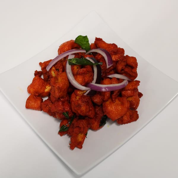 Curry On Indian Cuisine's Chicken 65, a vibrant red dish garnished with red onions and curry leaves.